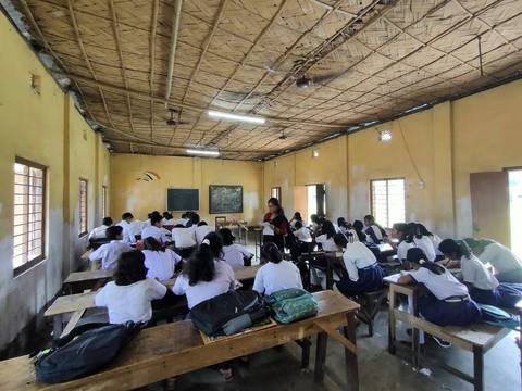 A teacher taking a lesson while students sit at long wooden benches
