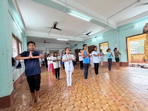 Children standing in rows with palms joined during a yoga session indoors